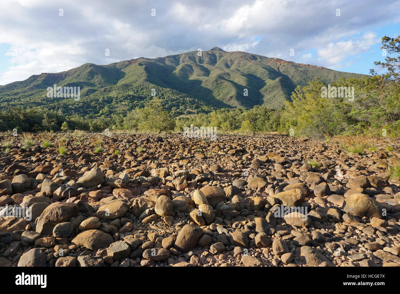 Dry riverbed with rocks and a mountain in background, New Caledonia, Dumbea river, Grande Terre island, south Pacific Stock Photo