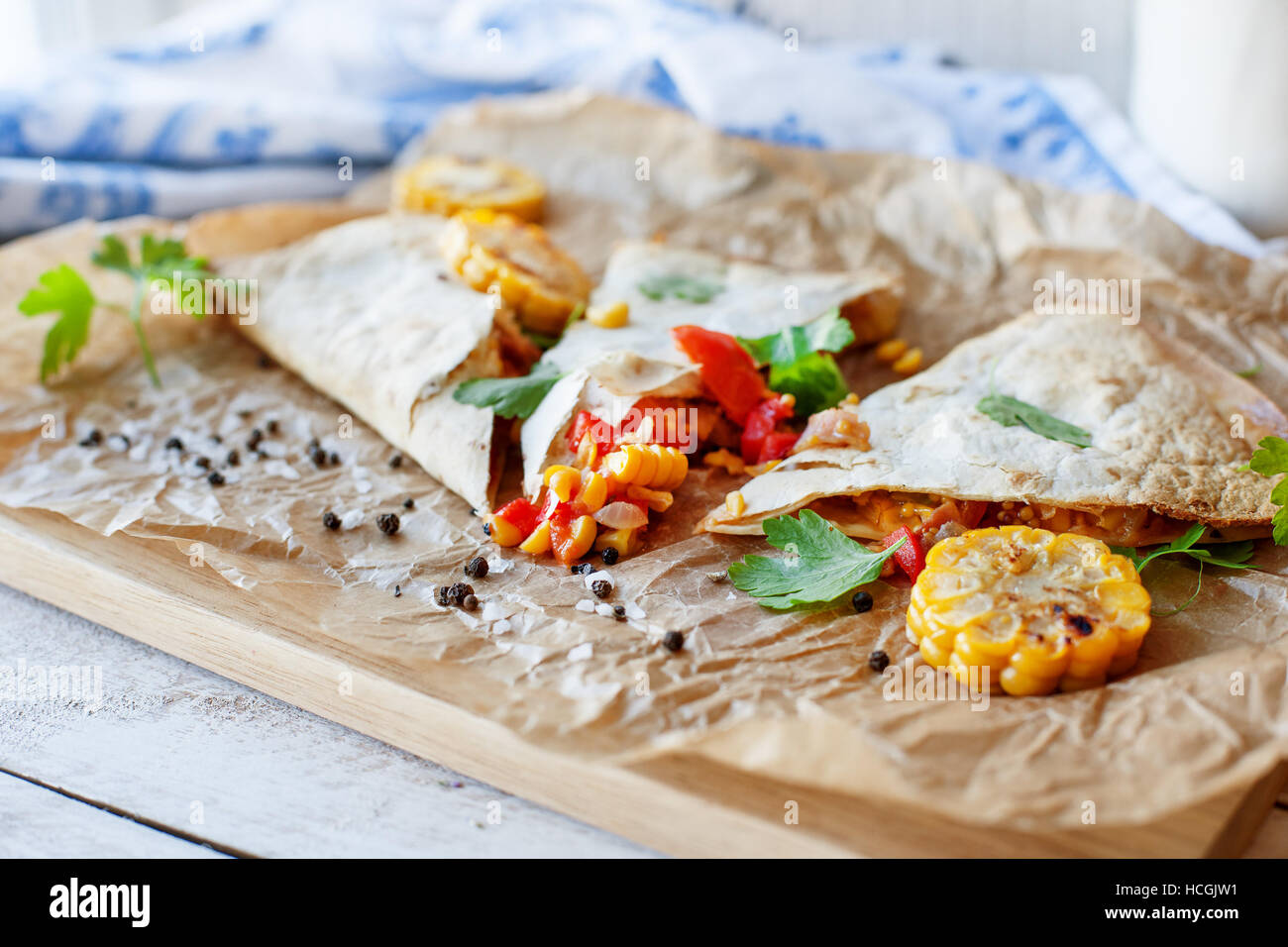 Mexican Quesadilla wrap with vegetables, corn, sweet pepper and sauces on the parchment and table. horizontal view. Stock Photo