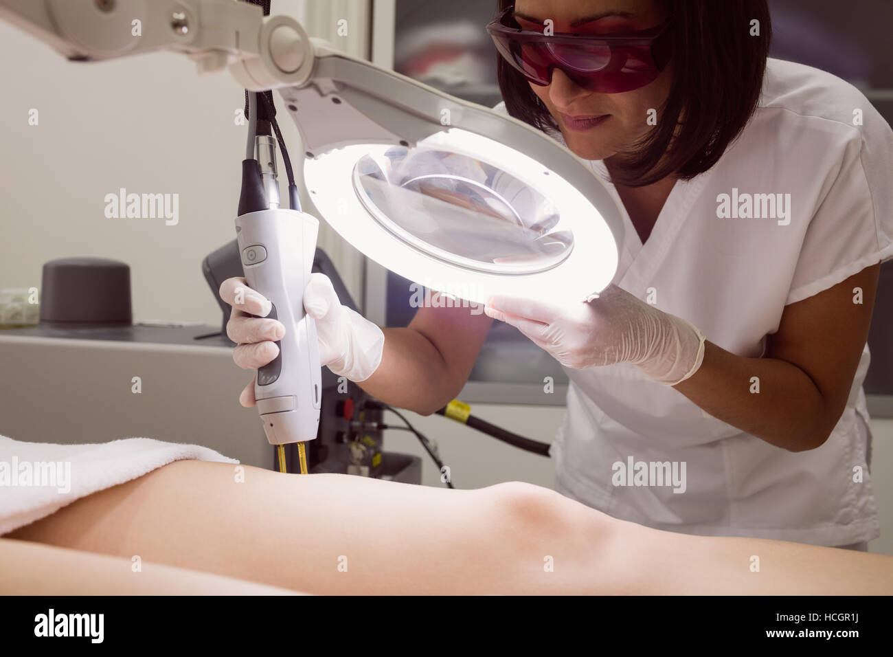 Doctor performing laser hair removal on female patient skin in clinic Stock Photo