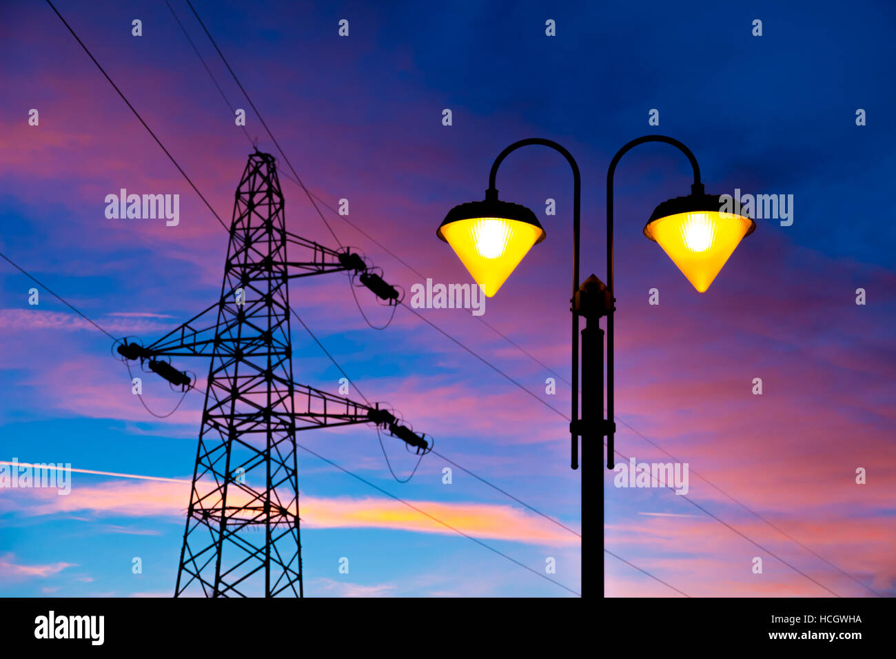 lit on streetlamp at sunset with high-tension line and pylon on the background Stock Photo