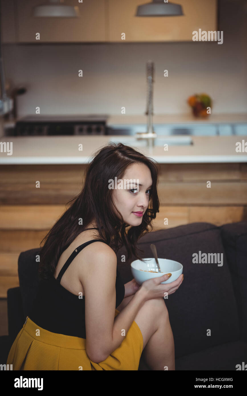 Woman sitting on sofa eating breakfast cereal in living room Stock Photo