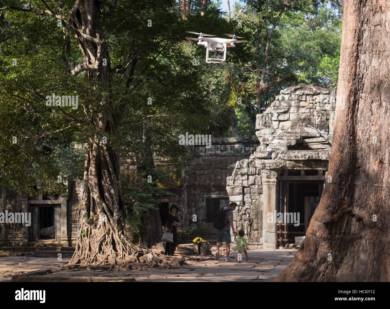 A western male tourist flying a drone at the Ta Prohm temple as three tourists look on in Siem Reap, Cambodia. Stock Photo