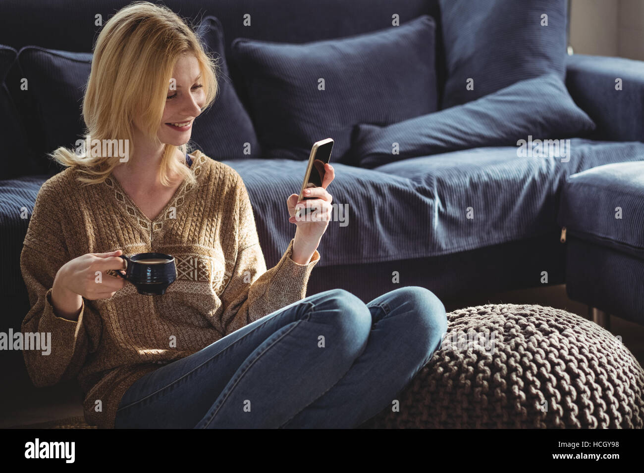 Beautiful woman using mobile phone while having tea in living room Stock Photo