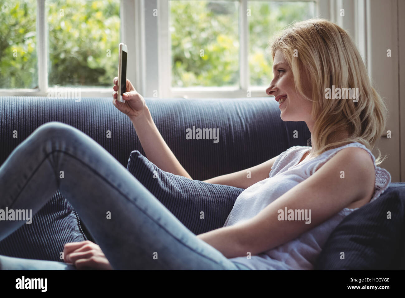 Beautiful woman sitting on sofa and using mobile phone in living room Stock Photo