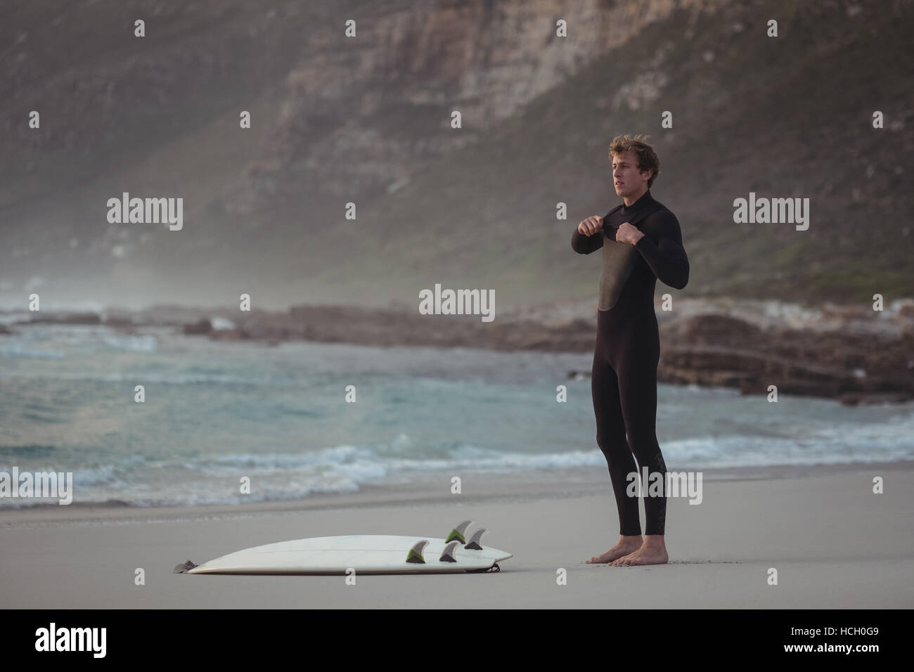 Man wearing wetsuit standing on beach Stock Photo
