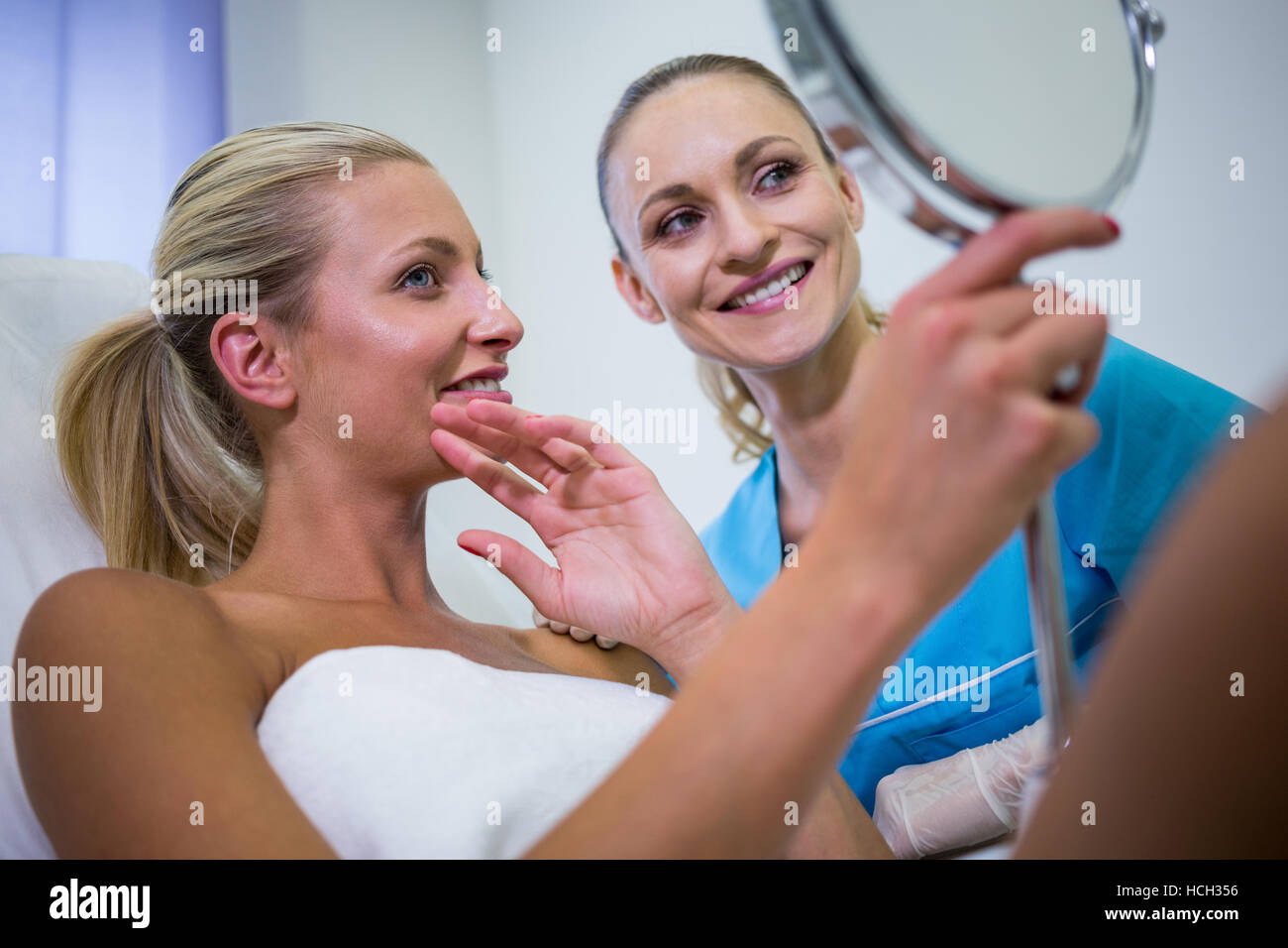 Woman checking her skin in the mirror after receiving cosmetic treatment Stock Photo