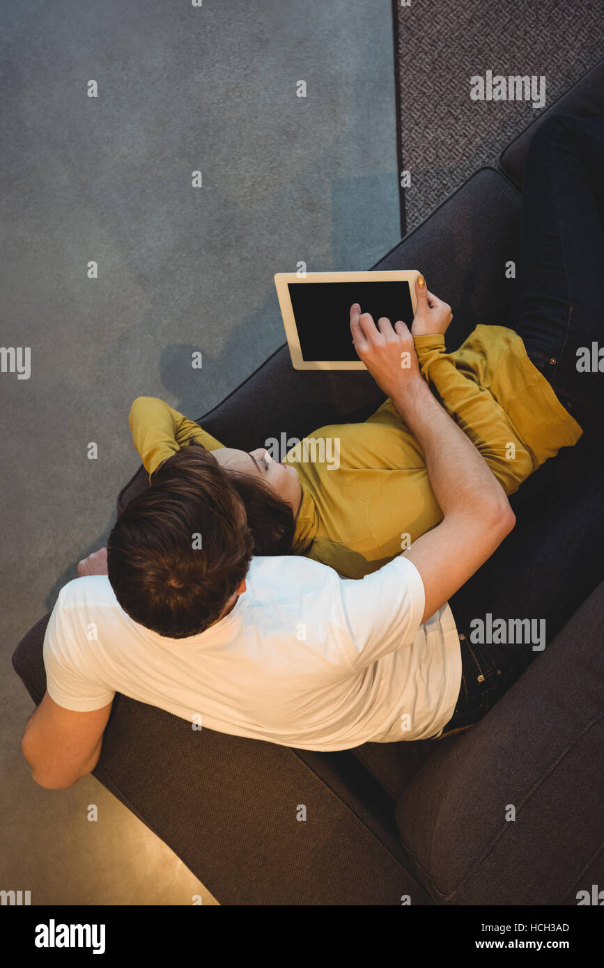 Cheerful couple lying together on sofa using digital tablet Stock Photo