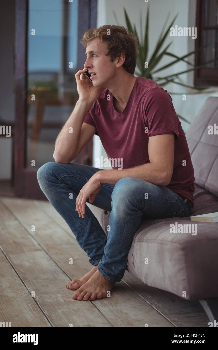 Man sitting on sofa and talking on mobile phone Stock Photo