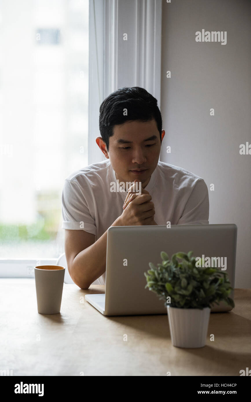Man looking at laptop with a cup of coffee on table Stock Photo
