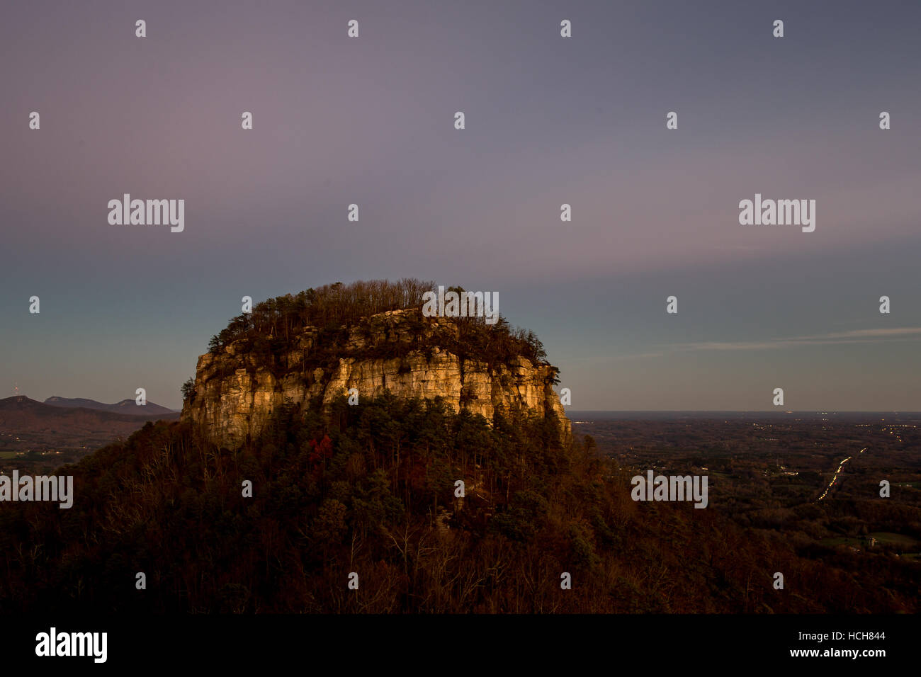 Big Pinnacle of Pilot Mountain in North Carolina, USA with sunset pink clouds and lights from cars on a highway in the distance Stock Photo