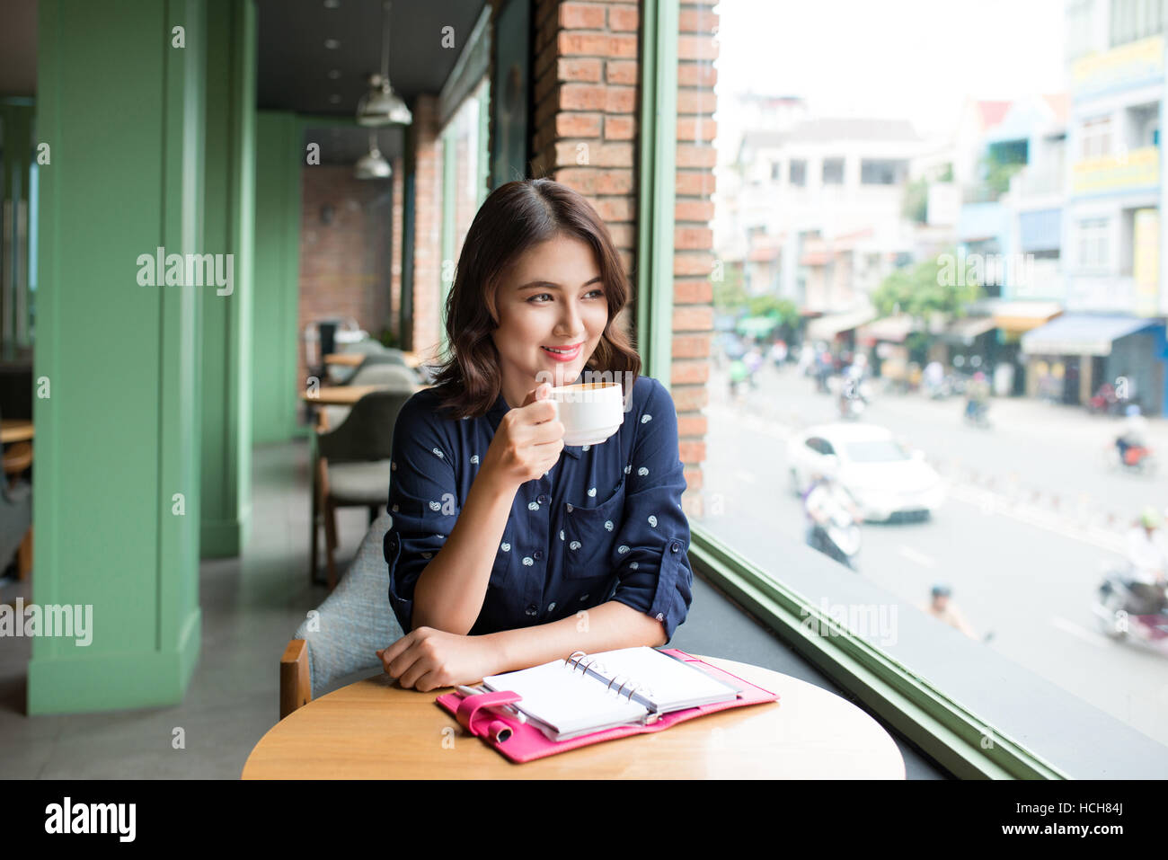Portrait of happy young business woman with mug in hands drinking coffee in the morning at restaurant Stock Photo