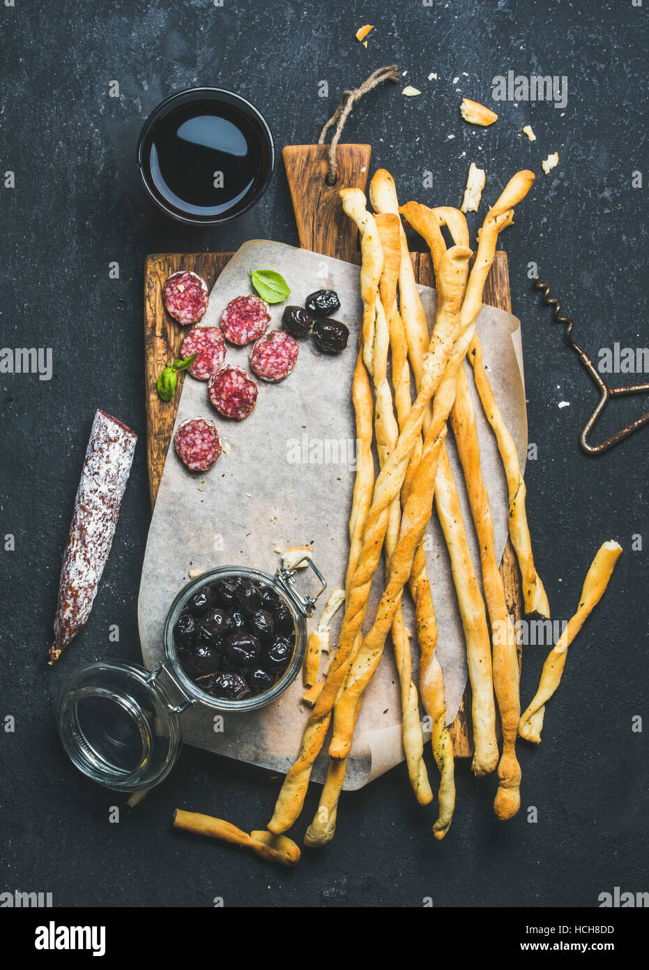 Wine and appetizers set. Italian Grissini bread sticks, dry cured pork meat sausage, black olives in jar and red wine in glass on wooden serving board Stock Photo