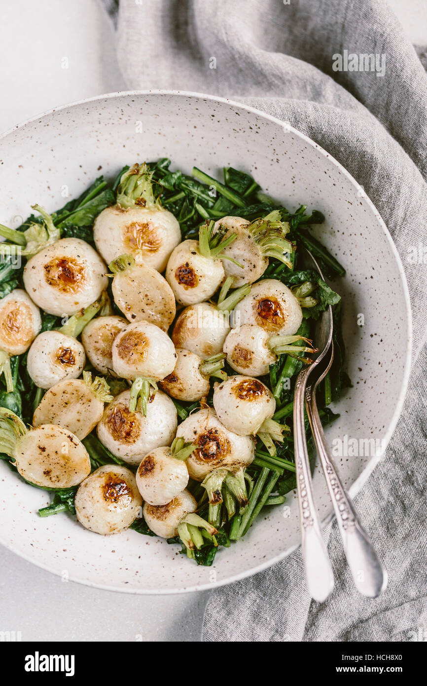 A bowl of roasted Japanese turnips (with their sauteed greens) are photographed from the top view. Stock Photo