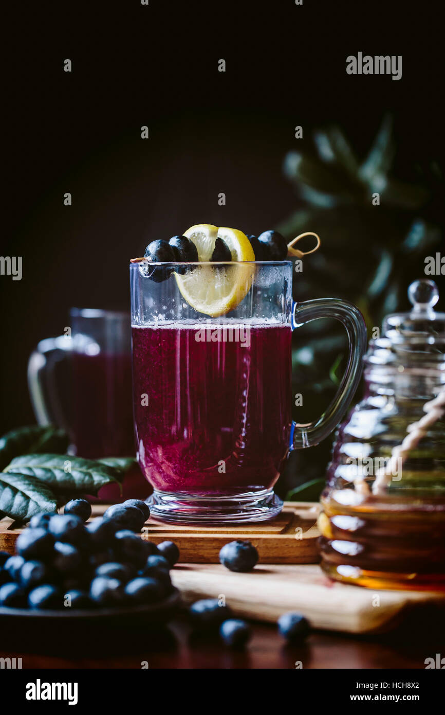 A glass of blueberry hot toddy garnished with lemon and blueberries is photographed from the front view. Stock Photo