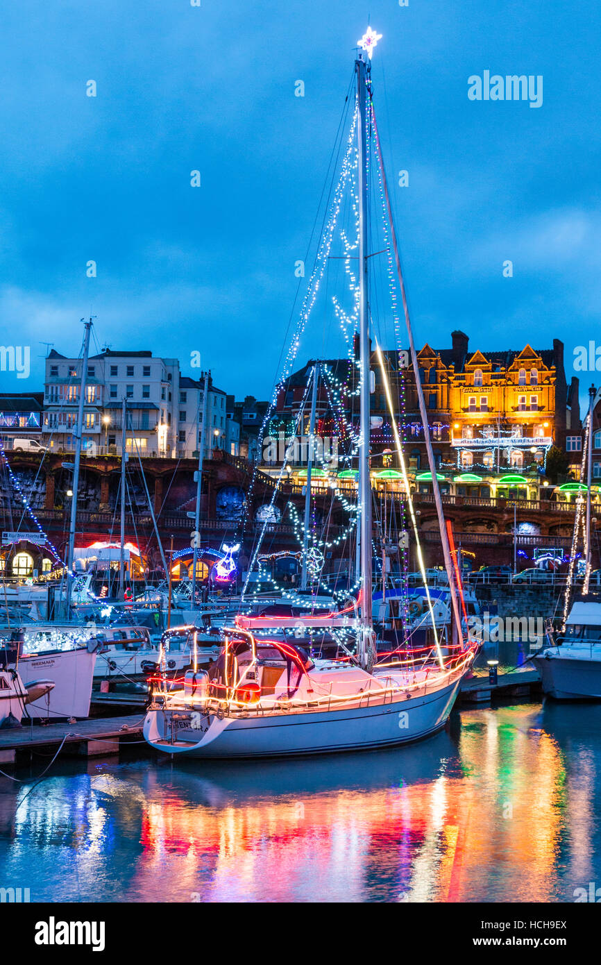 Ramsgate harbour in England. Seasonal Christmas lighting decorating various yachts and boats in the marina and buildings on the seafront. Blue hour. Stock Photo