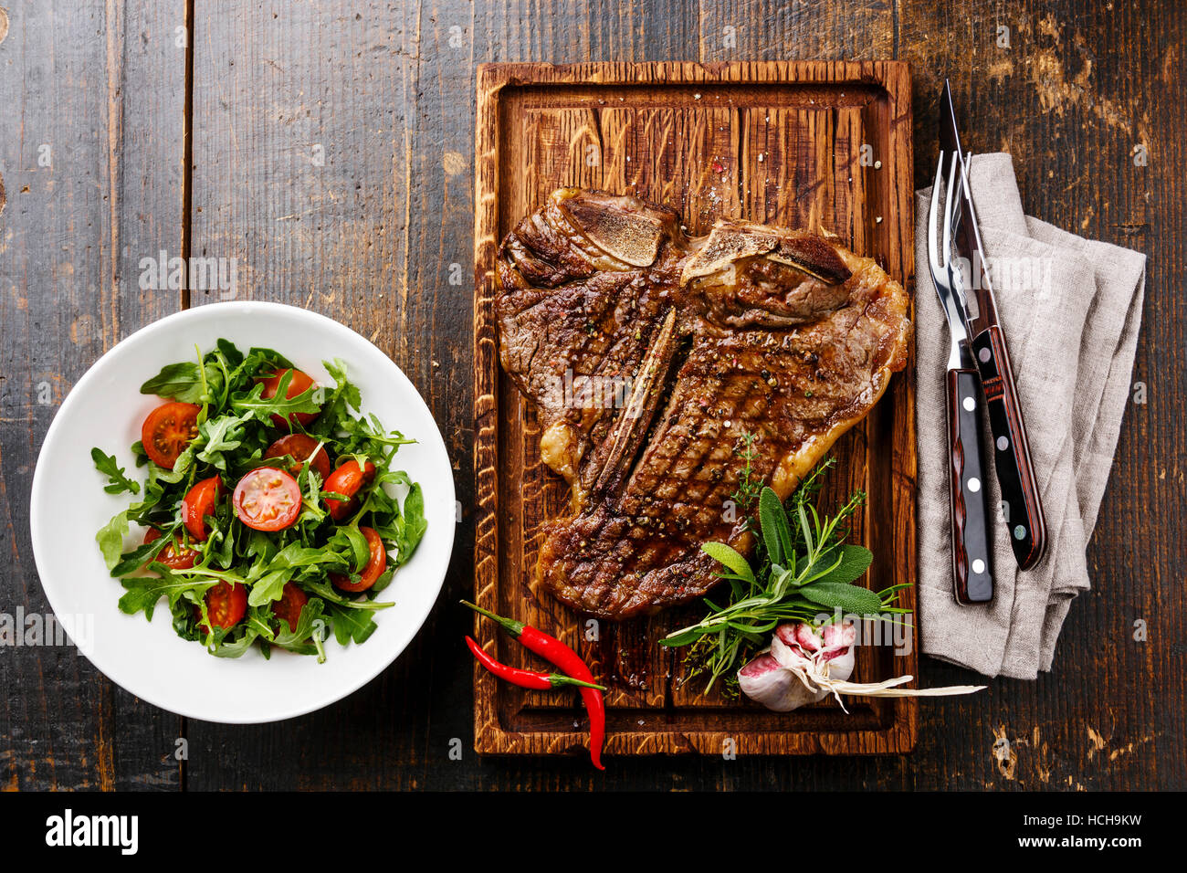 Grilled T-Bone Steak with Salad with Cherry tomatoes and Arugula on serving board on wooden background Stock Photo