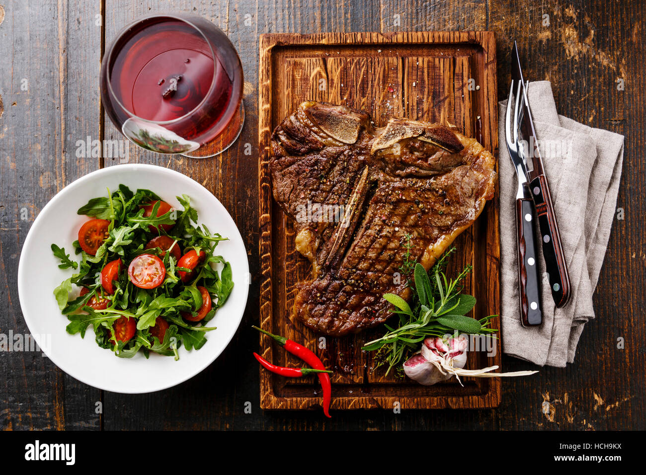 Grilled T-Bone Steak with Salad with Cherry tomatoes and Arugula on serving board on wooden background and red wine Stock Photo