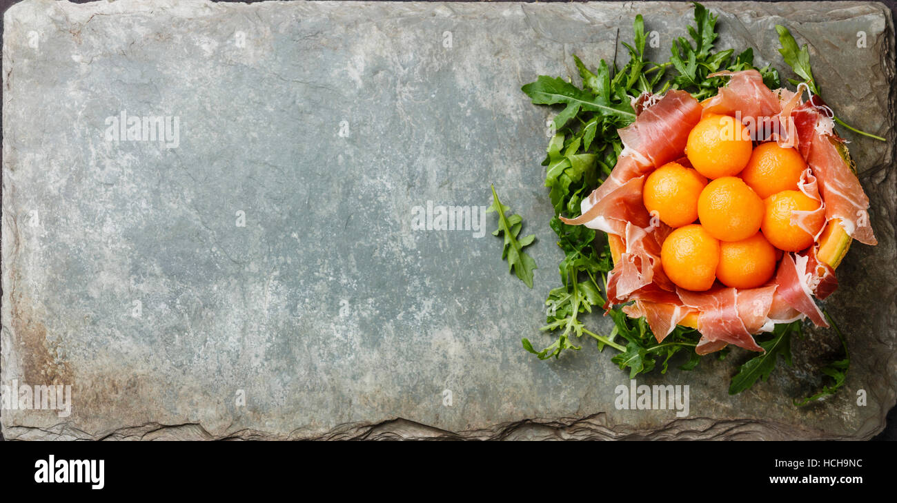 Prosciutto with Cantaloupe Melon balls and Arugula on stone slate background copy space Stock Photo