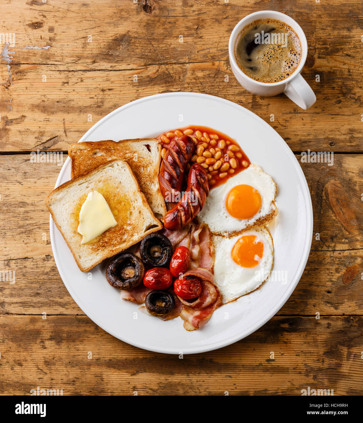 Full English Breakfast with fried eggs, sausages, bacon, beans, toasts, tomatoes and mushrooms on wooden background Stock Photo