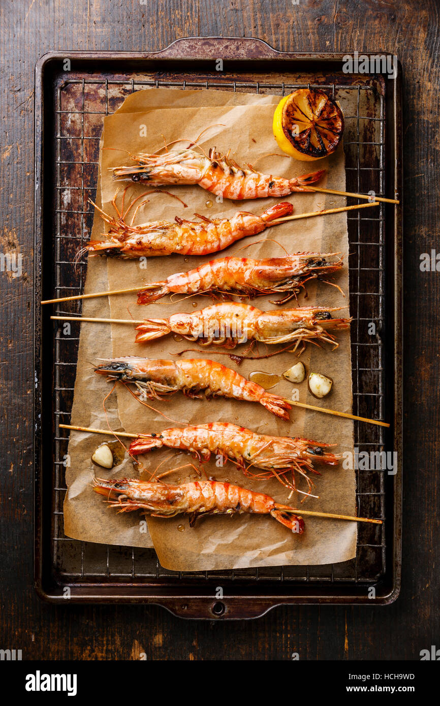 Grilled fried Tiger prawns shrimps on skewers and lemon on metal grid baking sheet background Stock Photo