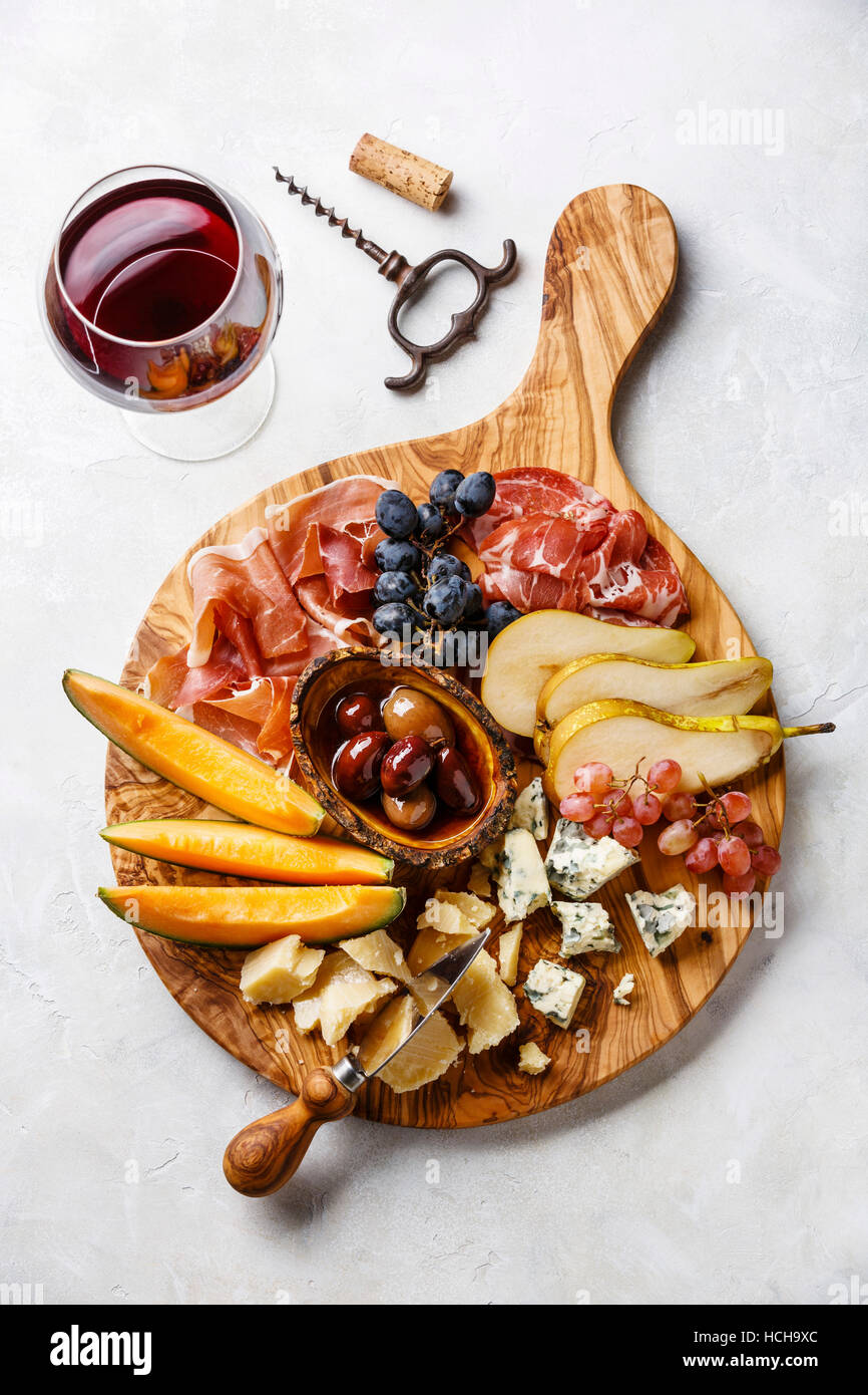 Meat and cheese plate antipasti snack with Prosciutto ham, Parmesan, Blue cheese, Cantaloupe melon and Olives on olive wood serving board on concrete Stock Photo