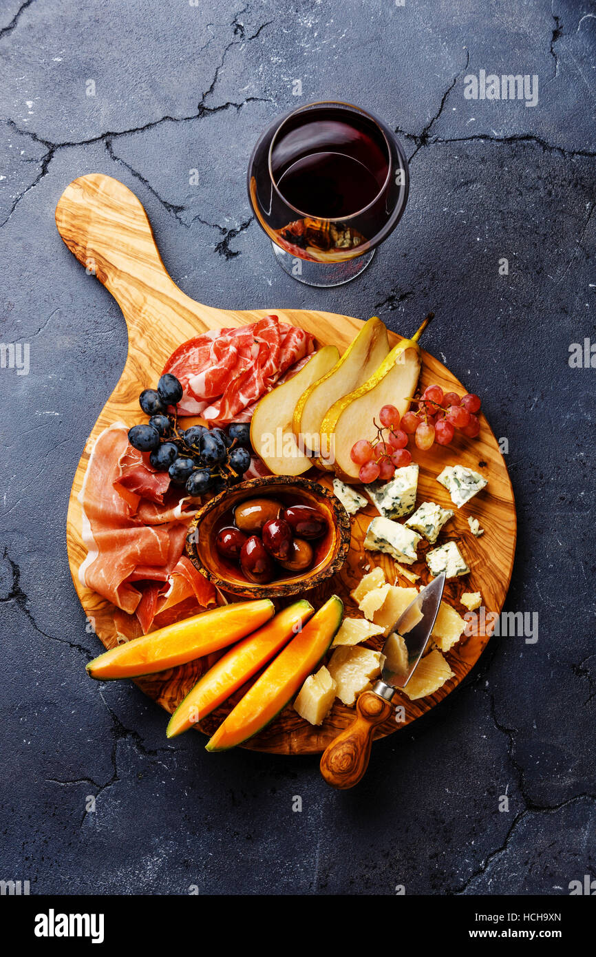 Meat and cheese plate antipasti snack with Prosciutto ham, Parmesan, Blue cheese, Cantaloupe melon and Olives on olive wood serving board on dark ston Stock Photo