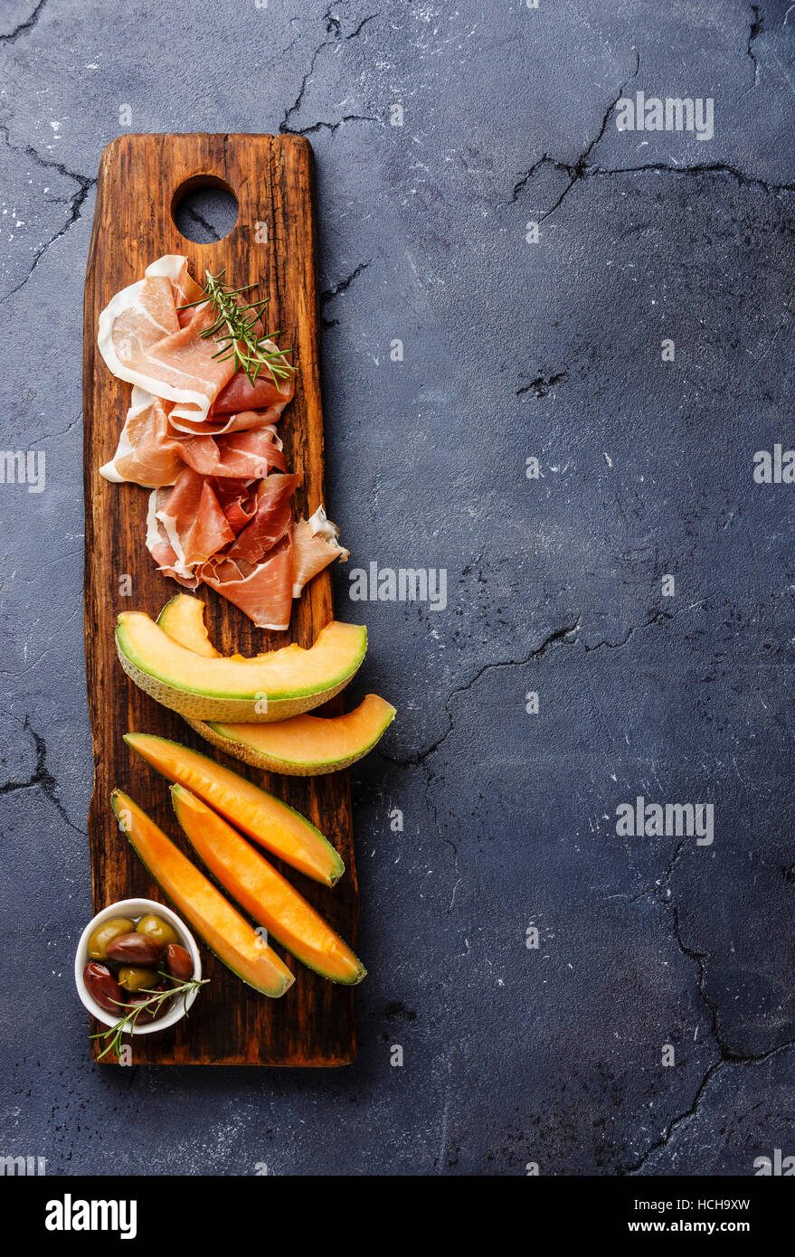 Meat plate antipasti snack with Prosciutto ham, cantaloupe melon and olives on dark stone background copy space Stock Photo