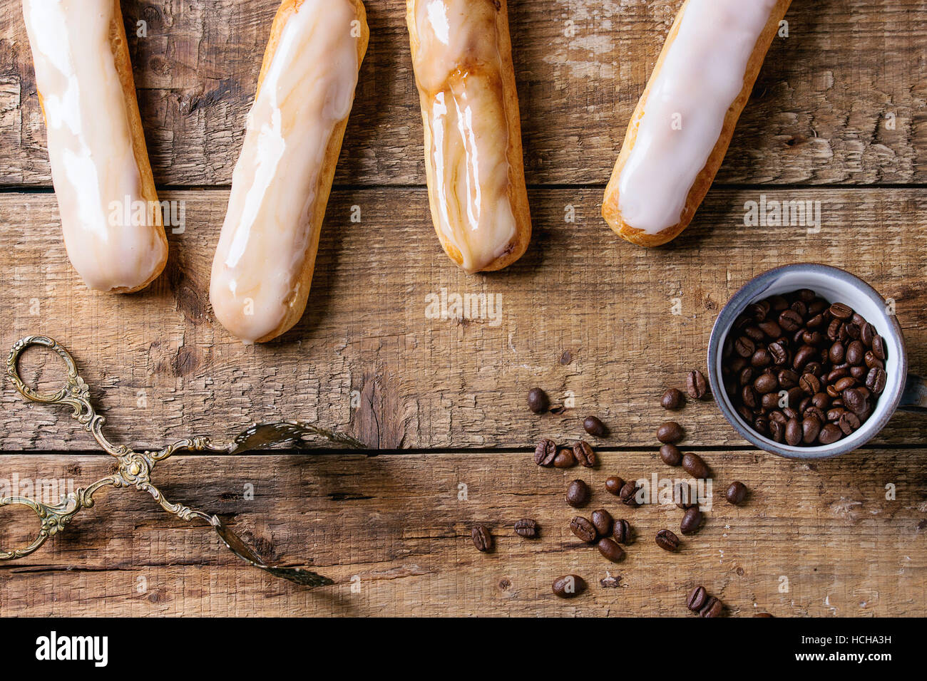 Fresh homemade Coffee eclairs with different glaze and coffee beans over old wooden texture background with space for text. Top view. Stock Photo