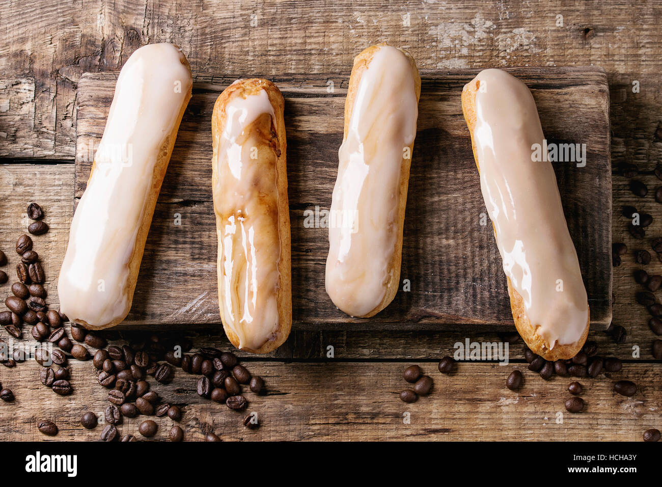 Fresh homemade Coffee eclairs with different glaze and coffee beans  on wood chopping board over old wooden texture background with space for text. To Stock Photo