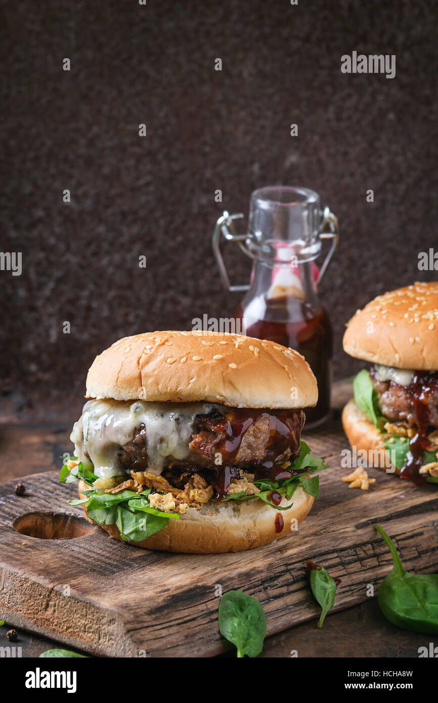 Two hamburgers with beef burger cutlet, fried onion, spinach, ketchup sauce and blue cheese in traditional buns, served on wood chopping board over da Stock Photo