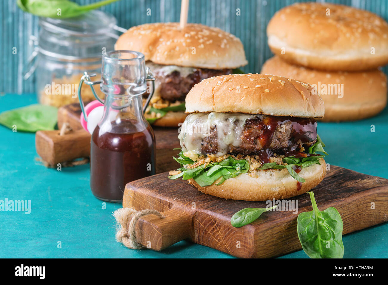 Two hamburgers with beef burger cutlet, fried onion, spinach, ketchup sauce and blue cheese in traditional buns, served on wood chopping board over br Stock Photo