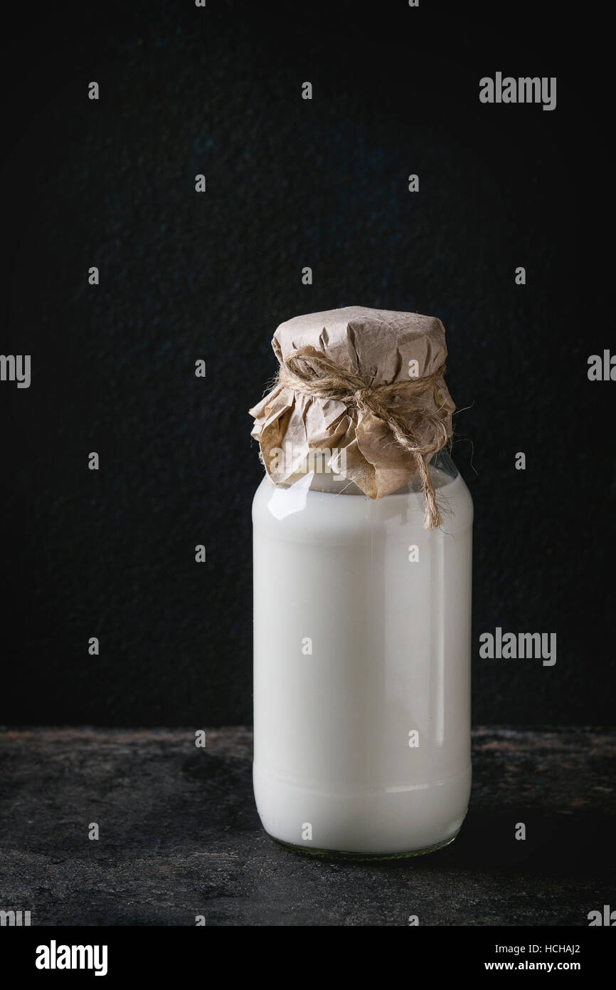 Glass bottle full of milk closed by paper and thread over black background. Copy space Stock Photo