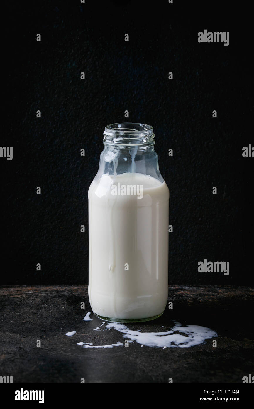 Opened glass bottle full of milk with milk spots over black background. Copy space Stock Photo