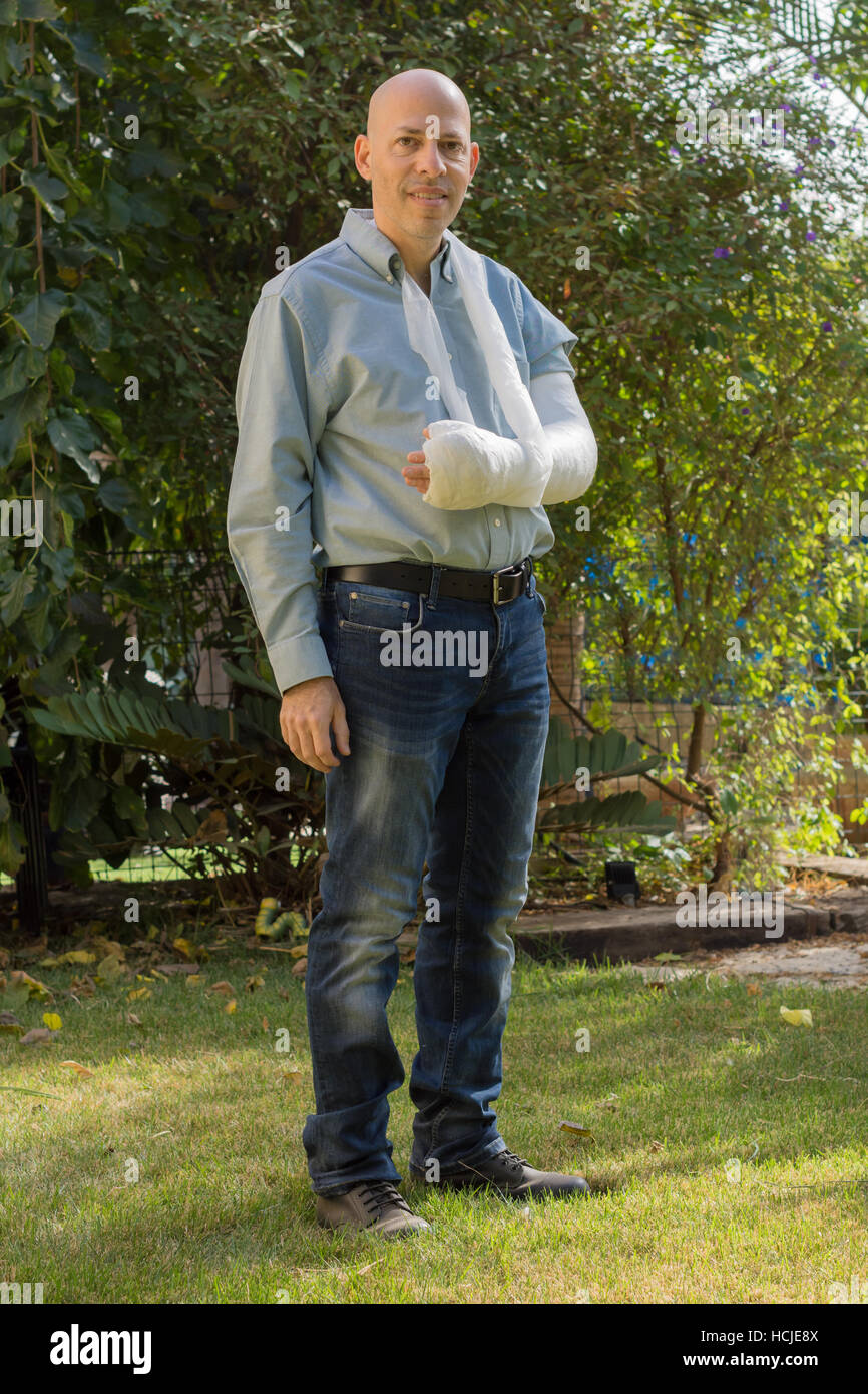 Young man with an arm and elbow in a white plaster / fiberglass getting some fresh air in the back yard Stock Photo