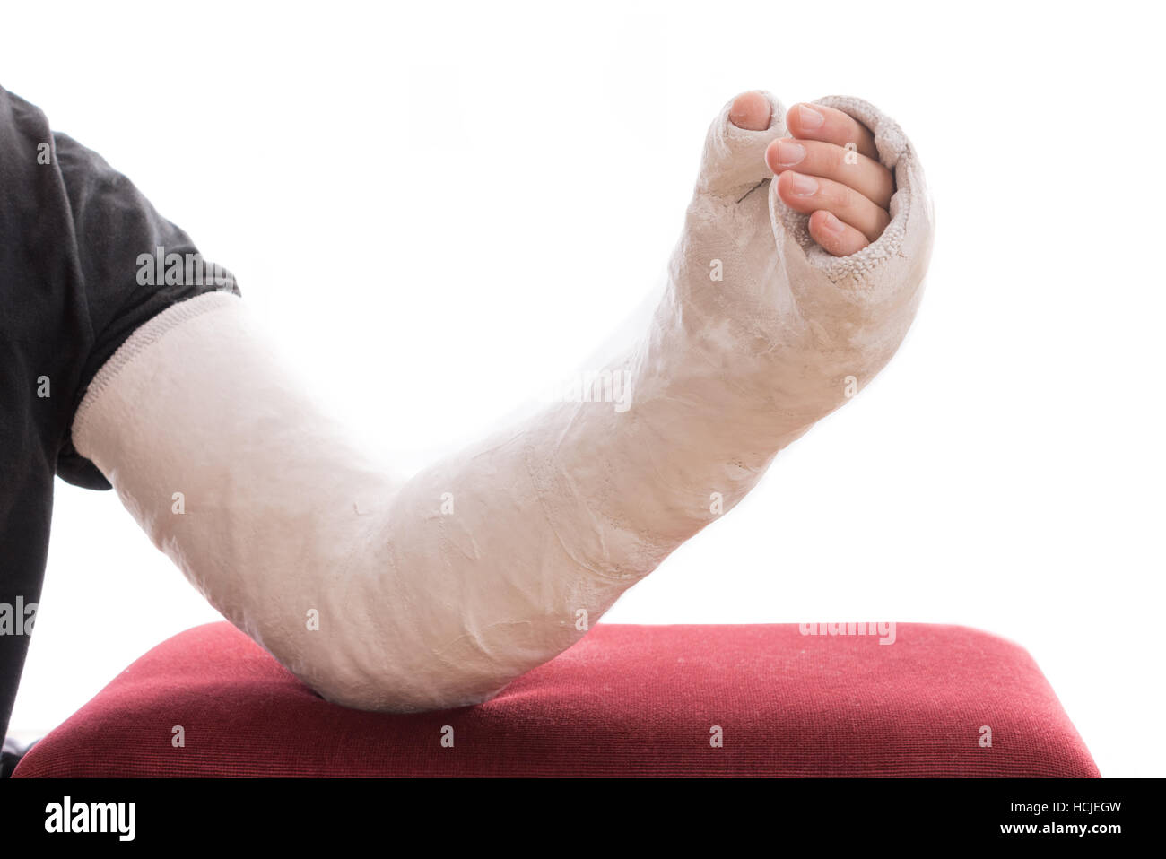 An old fashioned white long arm plasters cast covering the wrist, arm, and elbow, resting on an ottoman, isolated on white Stock Photo