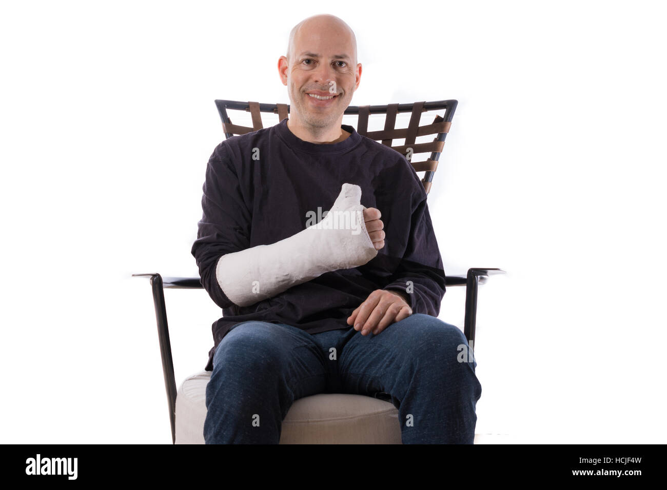Happy young man sitting on a couch making a thumbs up sign with his casted arm Stock Photo