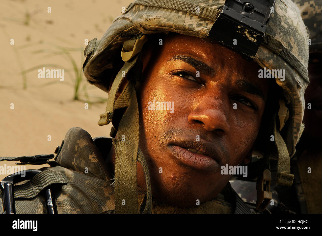 A soldiers covered in sweat and sand looks over his right shoulder. The