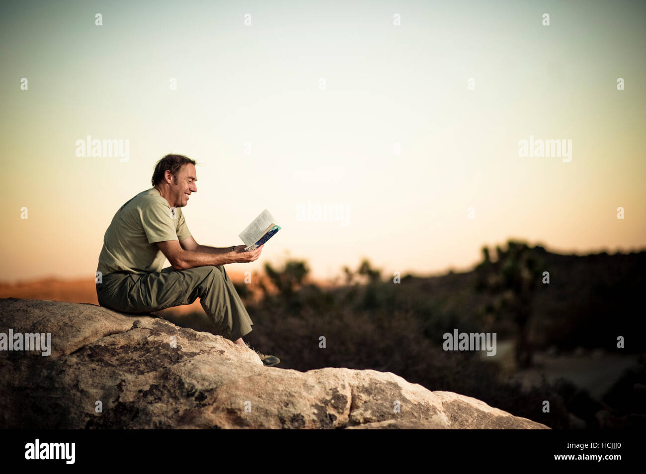 Roy Smith relaxes  with a good book atop a boulder in Joshua Tree, California at sunset. Stock Photo