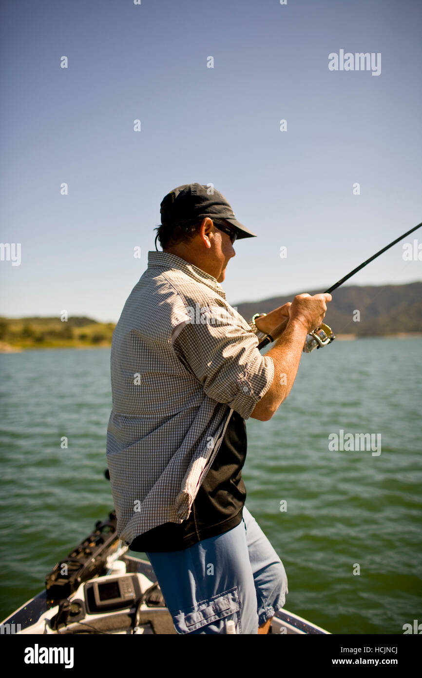 A man stands on a boat with fishing pole in hand while bass fishing in Lake Casitas Stock Photo