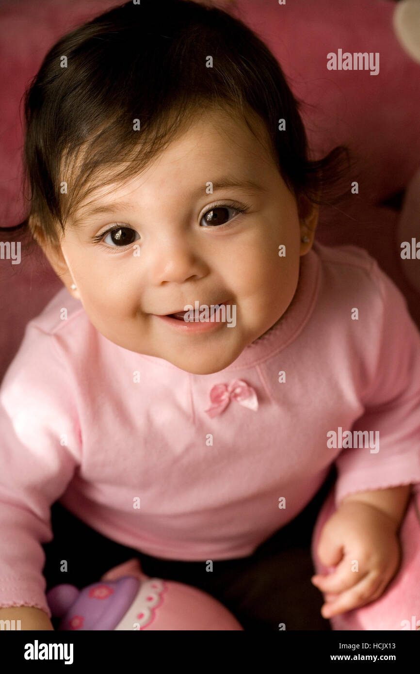 A wide, brown eyed baby girl smiles for the camera, wearing a soft A wide, brown eyed baby girl smiles for the camera, wearing a soft