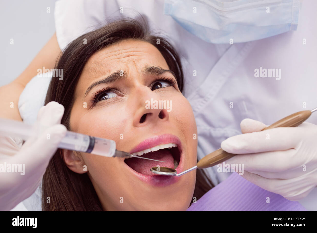 Dentist injecting anesthetics in scared female patient mouth Stock Photo