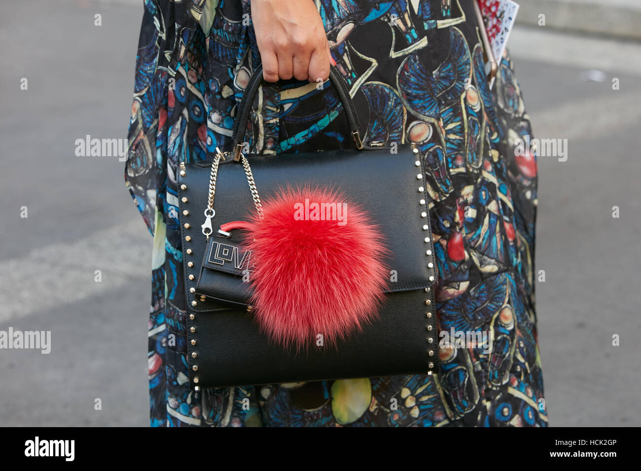 Woman with black leather bag with red fur decoration before Salvatore Ferragamo fashion show, Milan Fashion Week street style. Stock Photo