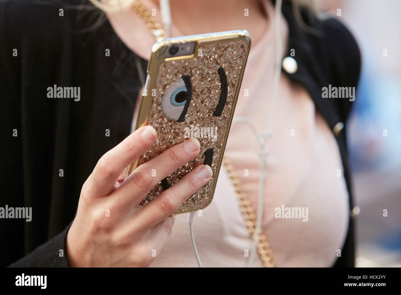 Woman with golden glitter smartphone cover with eyes before Salvatore Ferragamo fashion show, Milan Fashion Week street style. Stock Photo