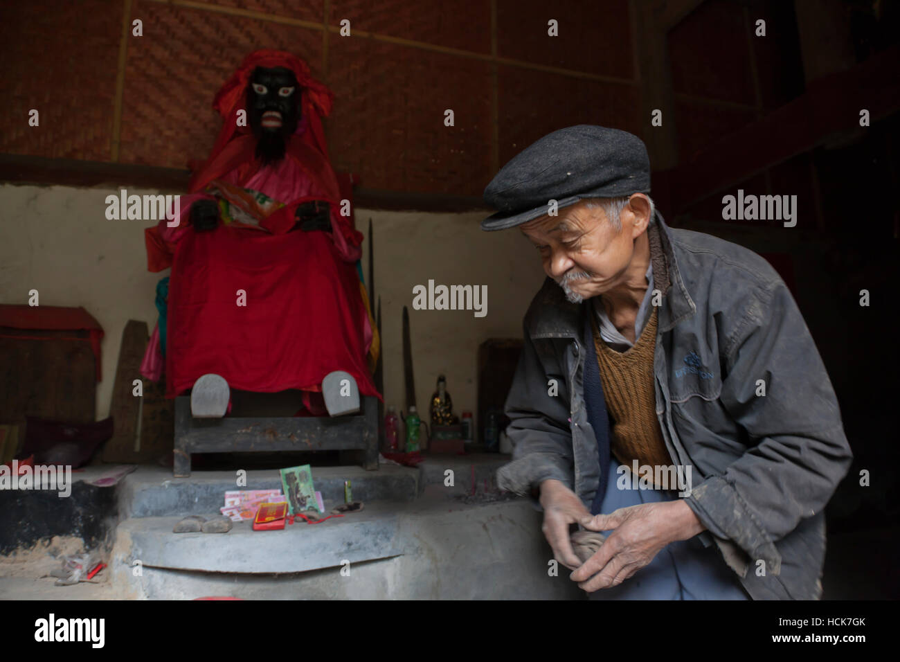 The caretaker of an old temple in a village in west China making merit and offerings to the mountain god, who was originally a Tibetan (hence the dark Stock Photo