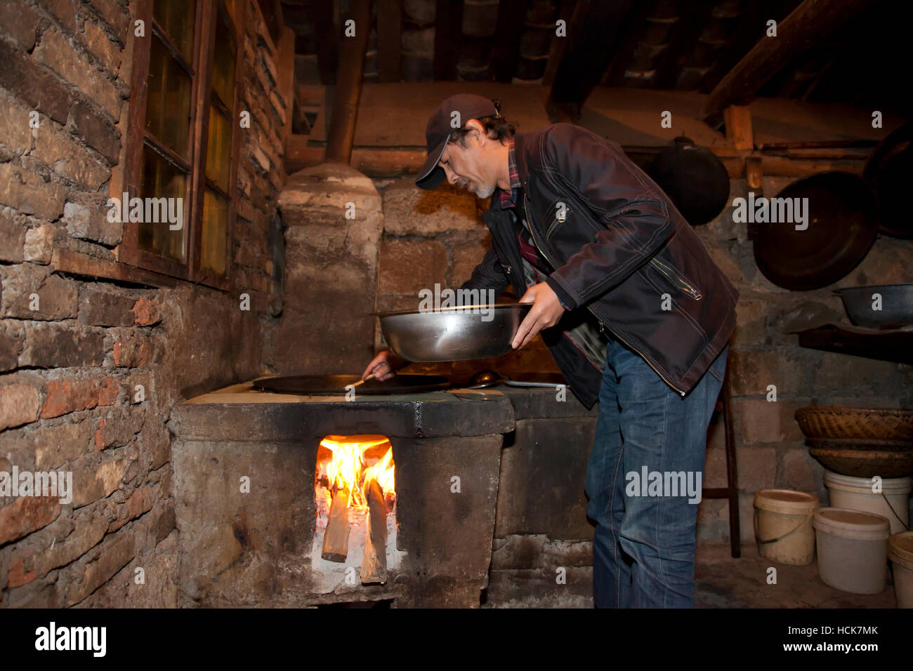 A man making a stirfry in the hearth with build-in wok in the kitchen of a farmhouse in a remote village in the mountains of west China. Stock Photo