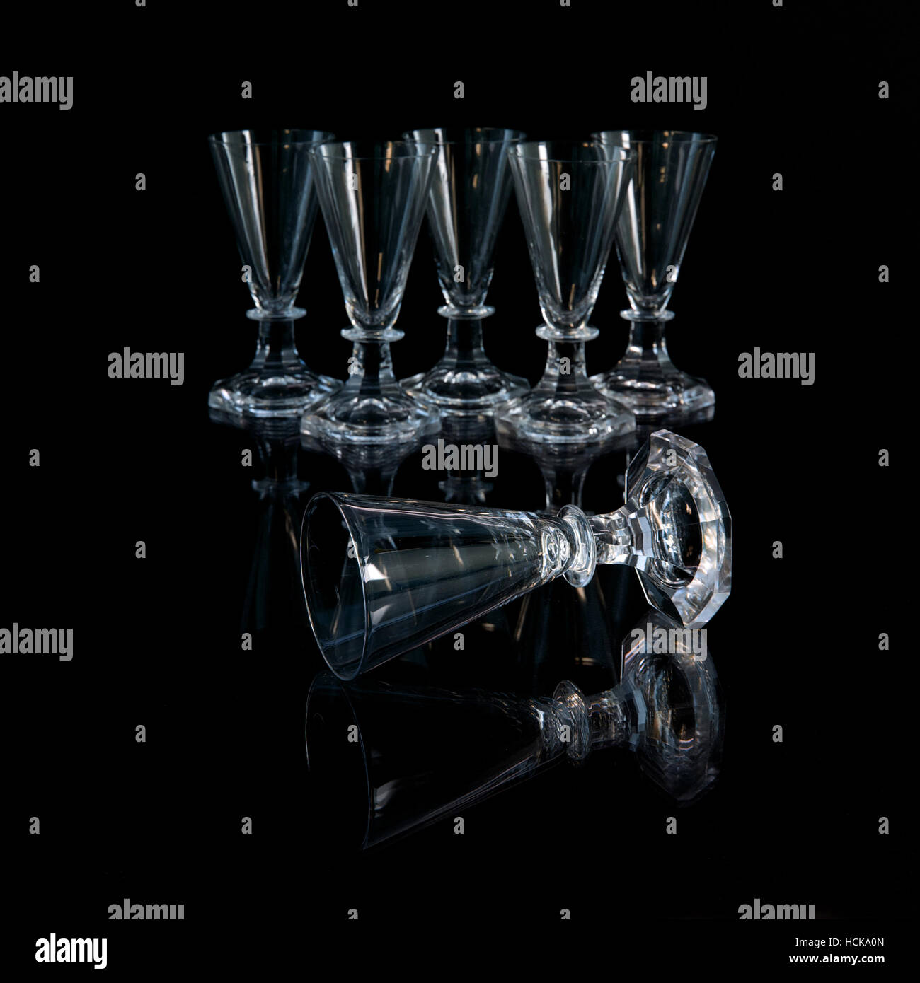 The six old crystal shot glasses where one is lying in front of the others in a black background Stock Photo