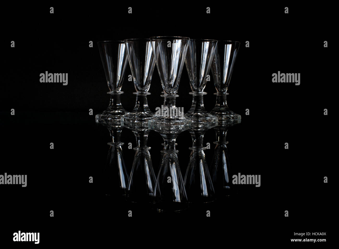 Six beautiful old crystal shot glasses on a glass plate with a black background Stock Photo