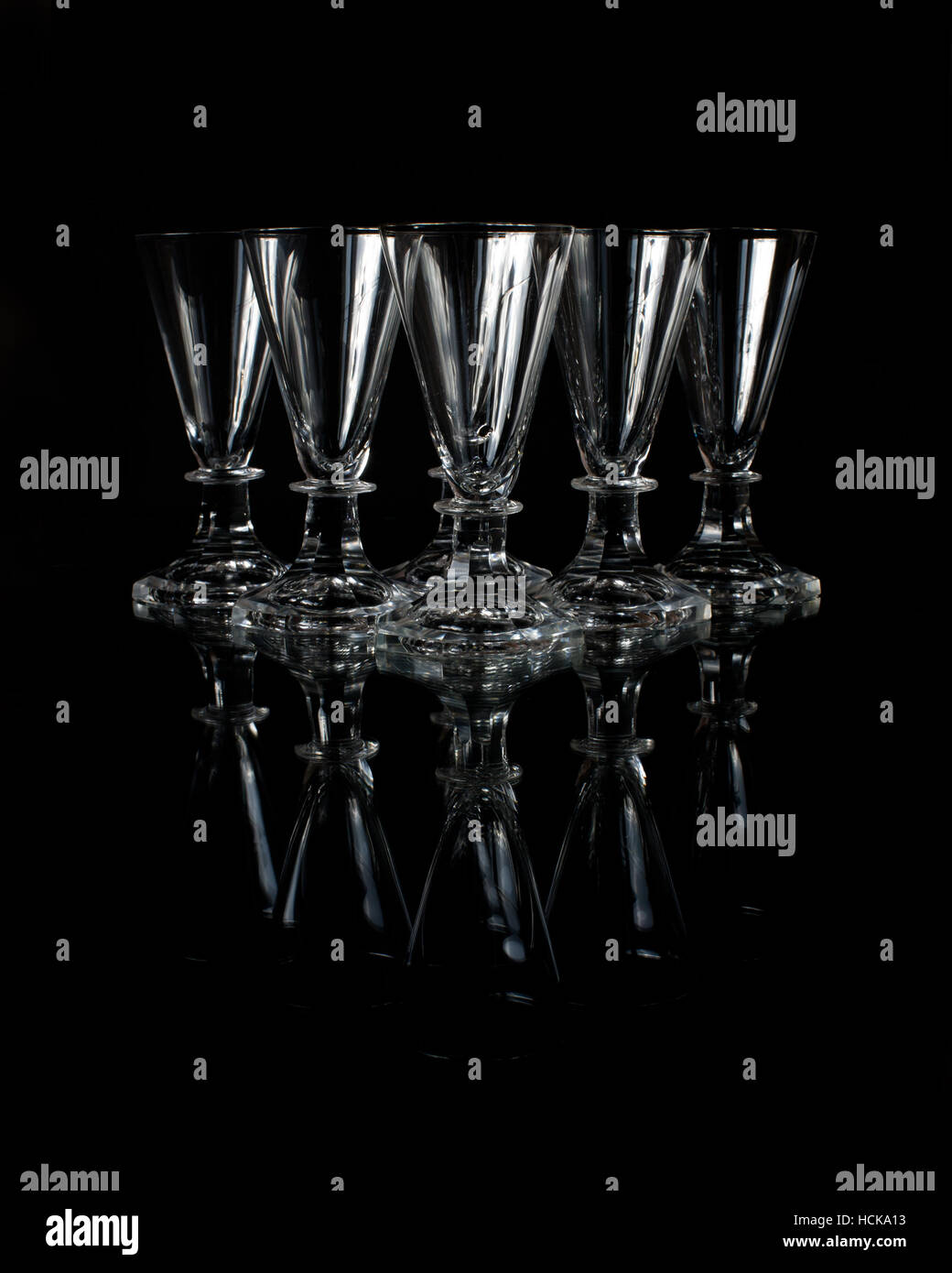 The six old crystal shot glasses on a glass plate with a black background Stock Photo