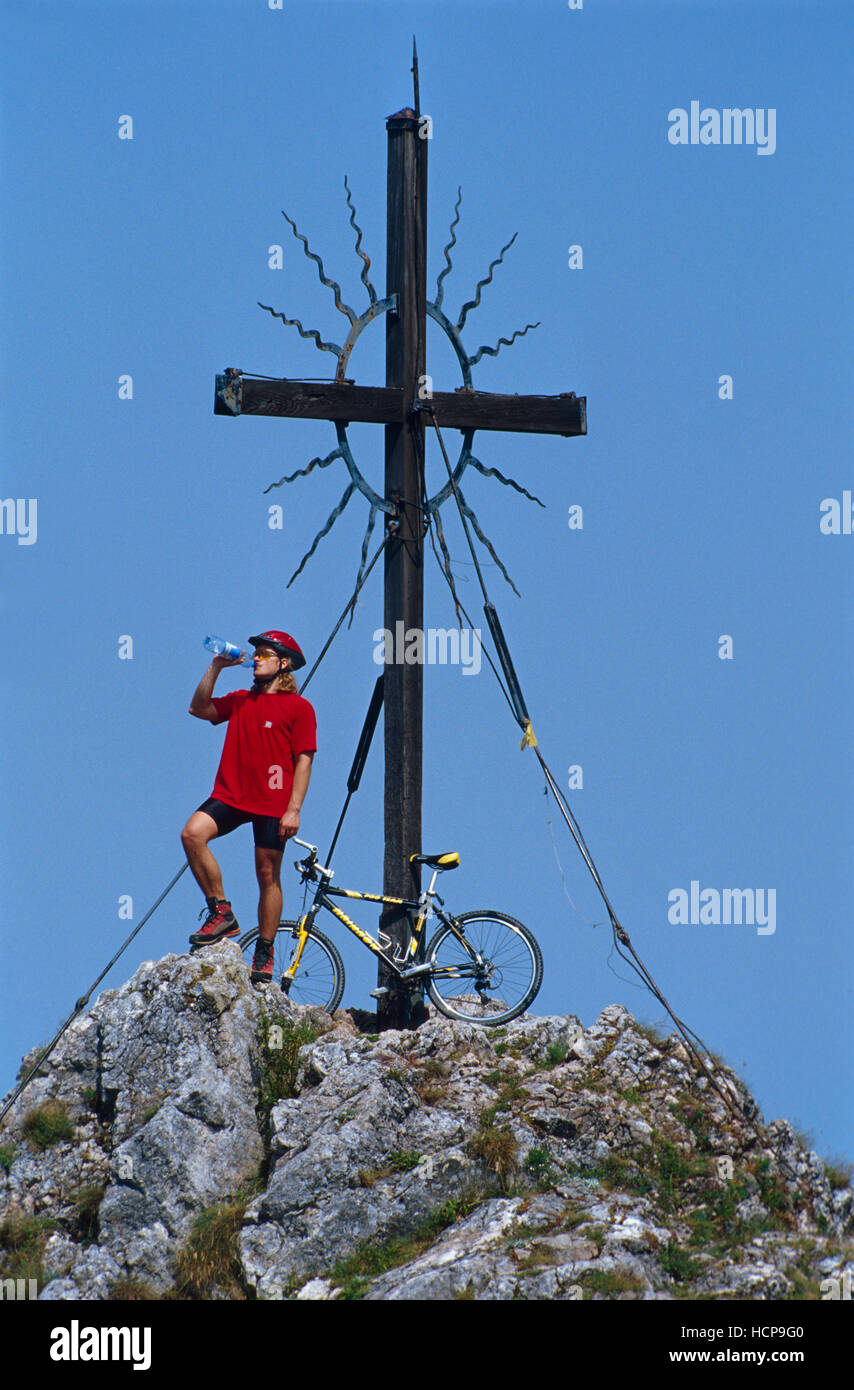 Cyclist with a mountainbike next to a cross on the summit of a hill, Steinerner Jaeger, Reichraming, Upper Austria, Austria Stock Photo