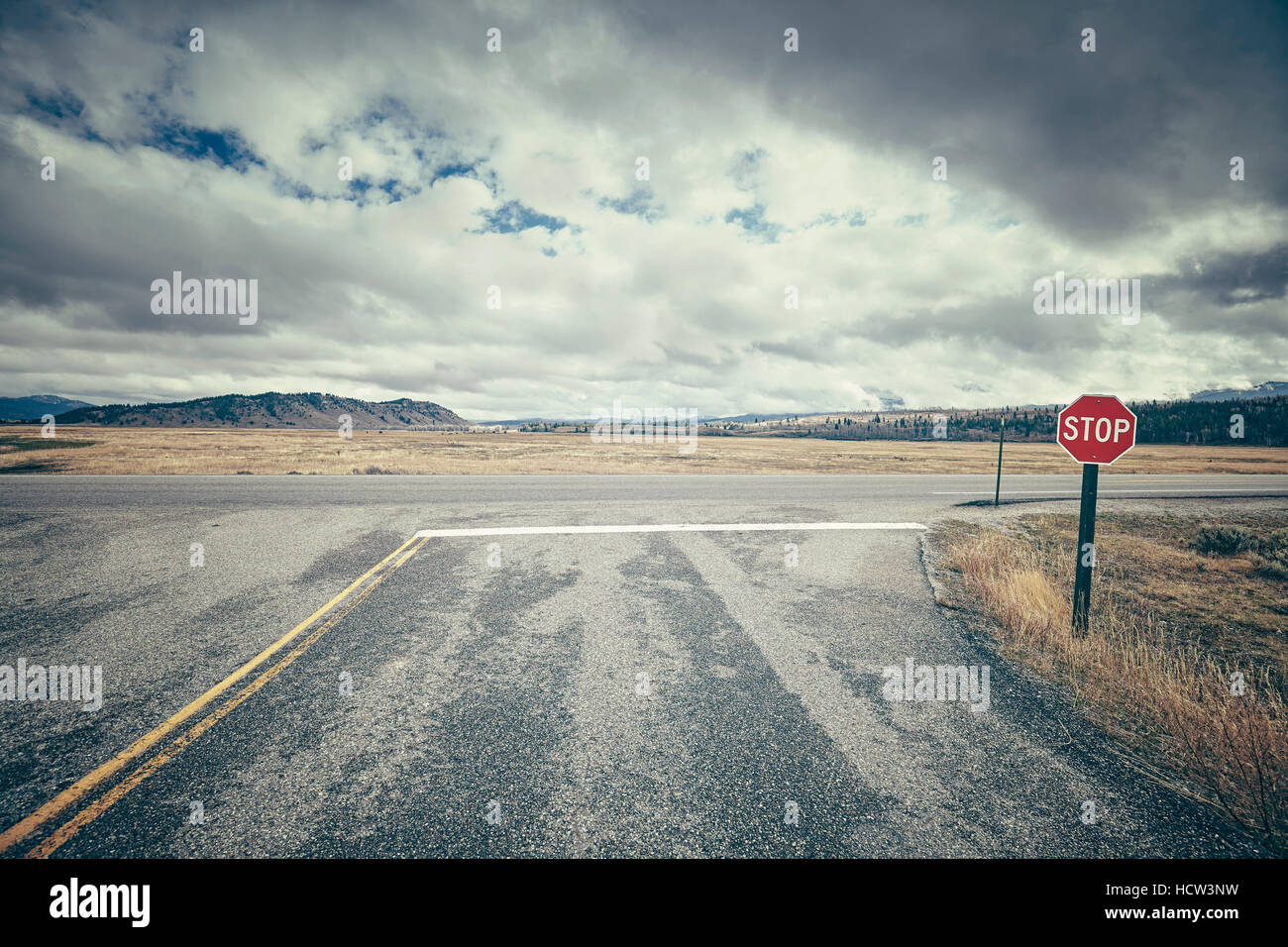Retro stylized road intersection with stop sign on a cloudy day, conceptual picture, USA. Stock Photo